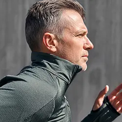 Man jogging outdoors, shown in profile, wearing a dark athletic jacket.