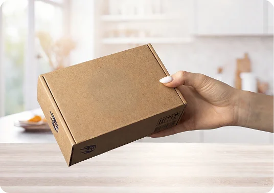 A hand holding a small brown cardboard box over a table against a blurred kitchen background